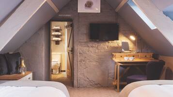 Une chambre confortable située sous les toits, avec un plafond en pente, un téléviseur fixé au mur, un bureau avec une chaise et un lit avec une table de chevet.