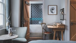 A room with a wooden desk, a chair, a small table with a bottle and glasses, a framed picture, and a view of a blue-tiled wall through an open door. - Haveners (Fowey)