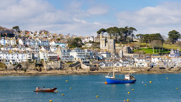 A coastal town with houses along the shore, a prominent church, and boats in the water. - Haveners (Fowey)