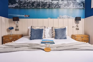Una cama bien tendida con vistas a un pueblo costero a través de un ventanal grande.