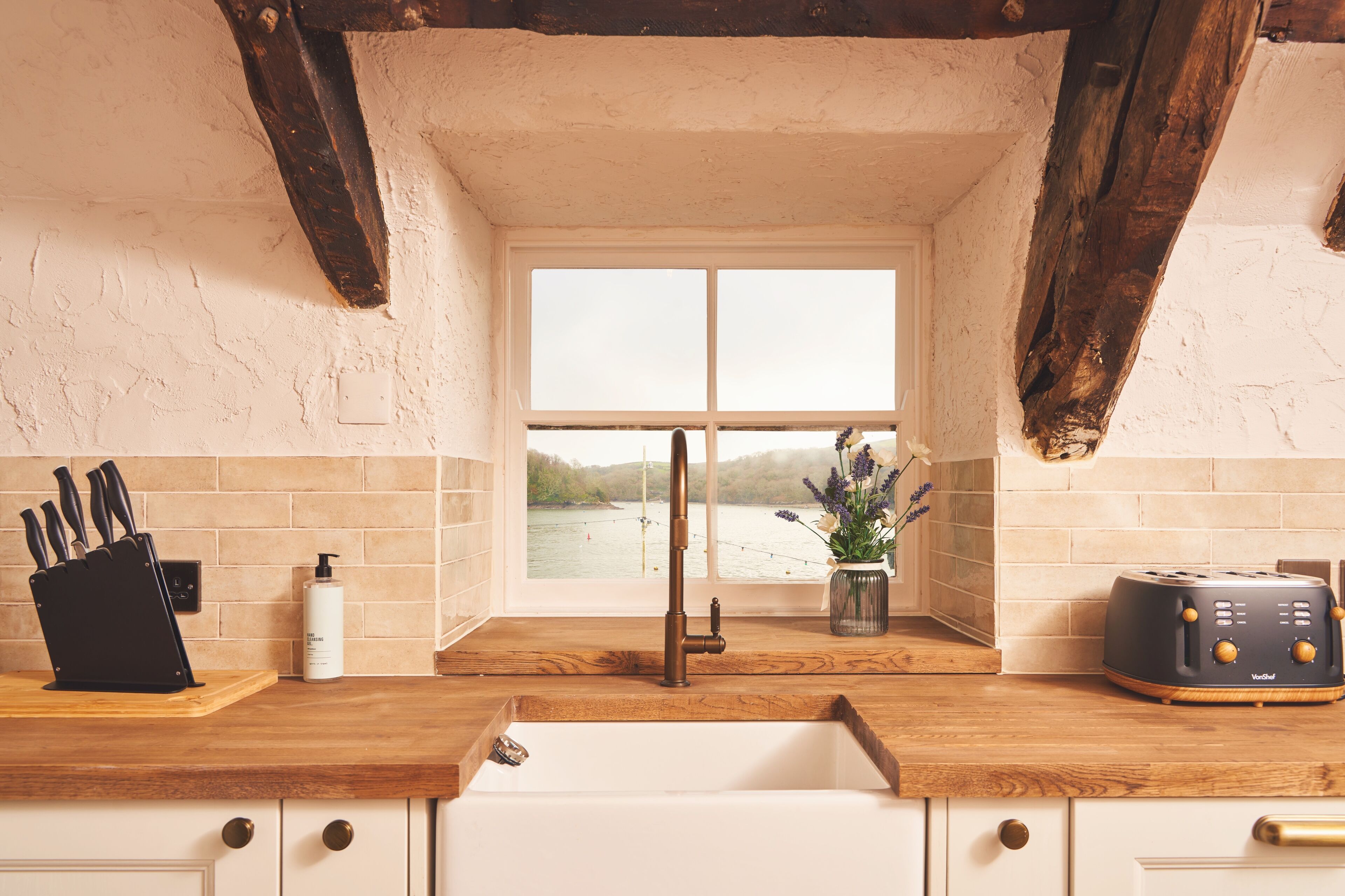 A kitchen with a wooden countertop, a sink, a window with a view of a lake, and a toaster.