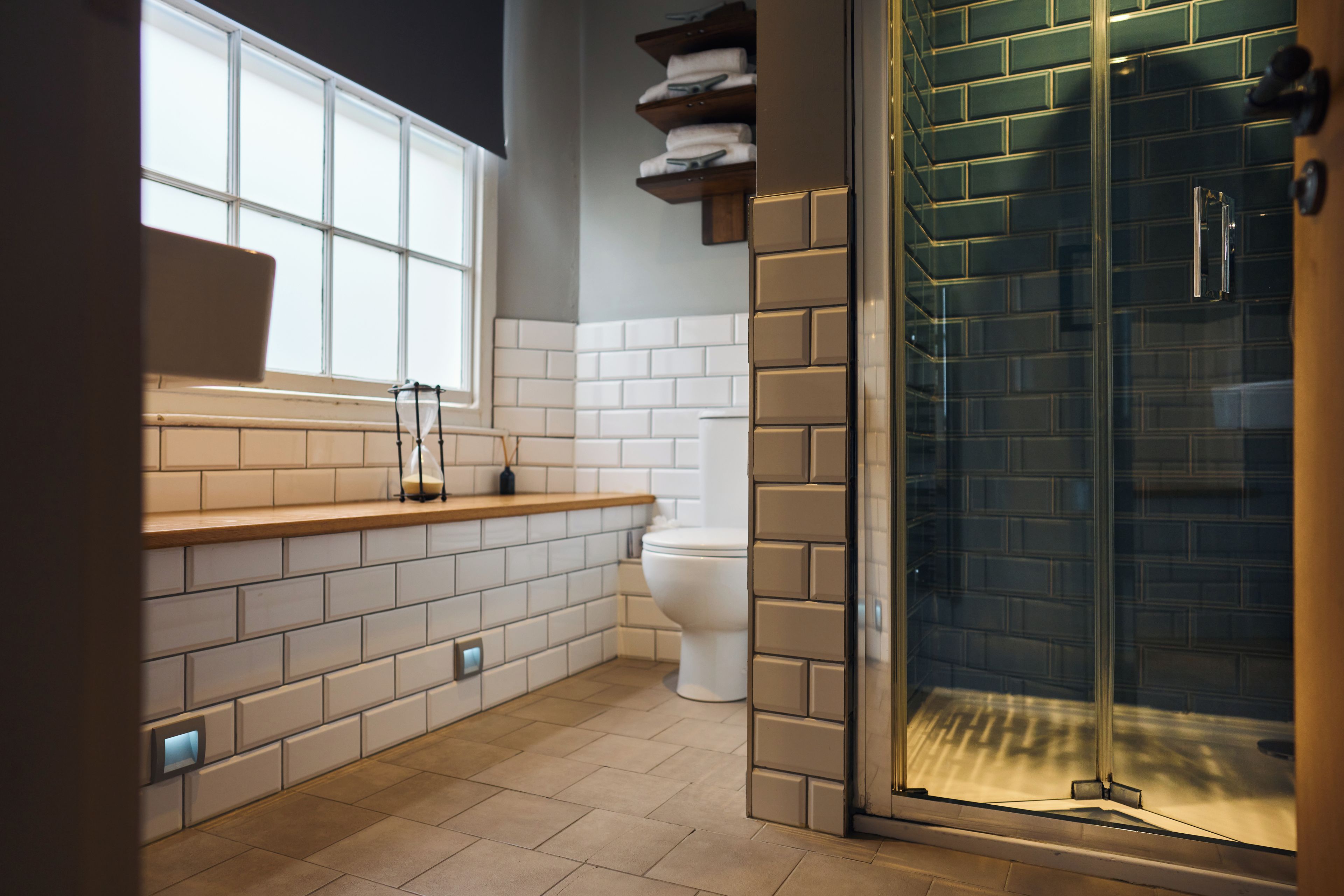 A modern bathroom with a glass shower enclosure, a toilet, and a sink area with a window.