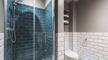 Une salle de bain avec une douche à parois de verre, des murs recouverts de carreaux blancs et des toilettes.