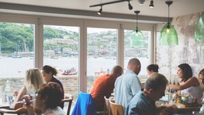 A restaurant with large windows offering a view of a harbor and buildings. - Haveners (Fowey)