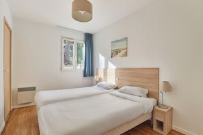 Een slaapkamer met twee bedden, een raam met gordijnen, een bedlampje en een aan de muur bevestigd schilderij.