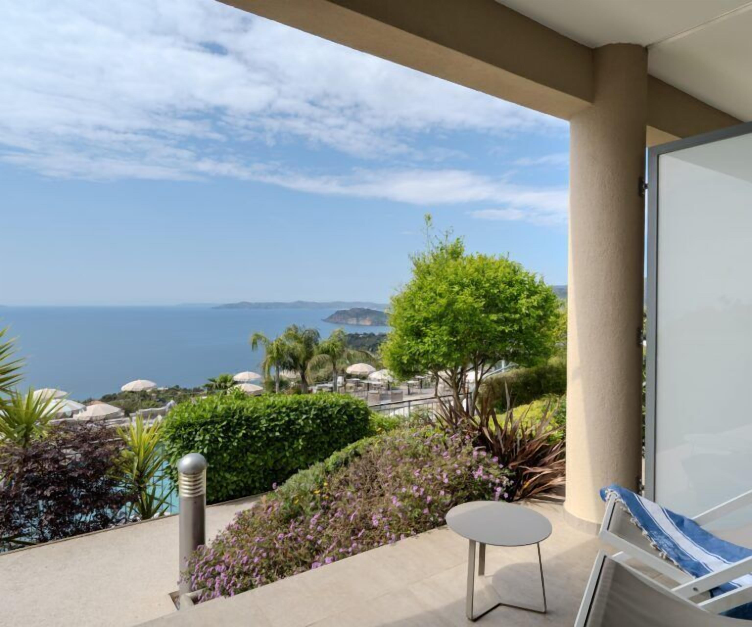 A balcony with a view of the sea, a small table, and a chair.