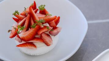 A dessert on a white plate with a white spoon containing red sauce beside it.