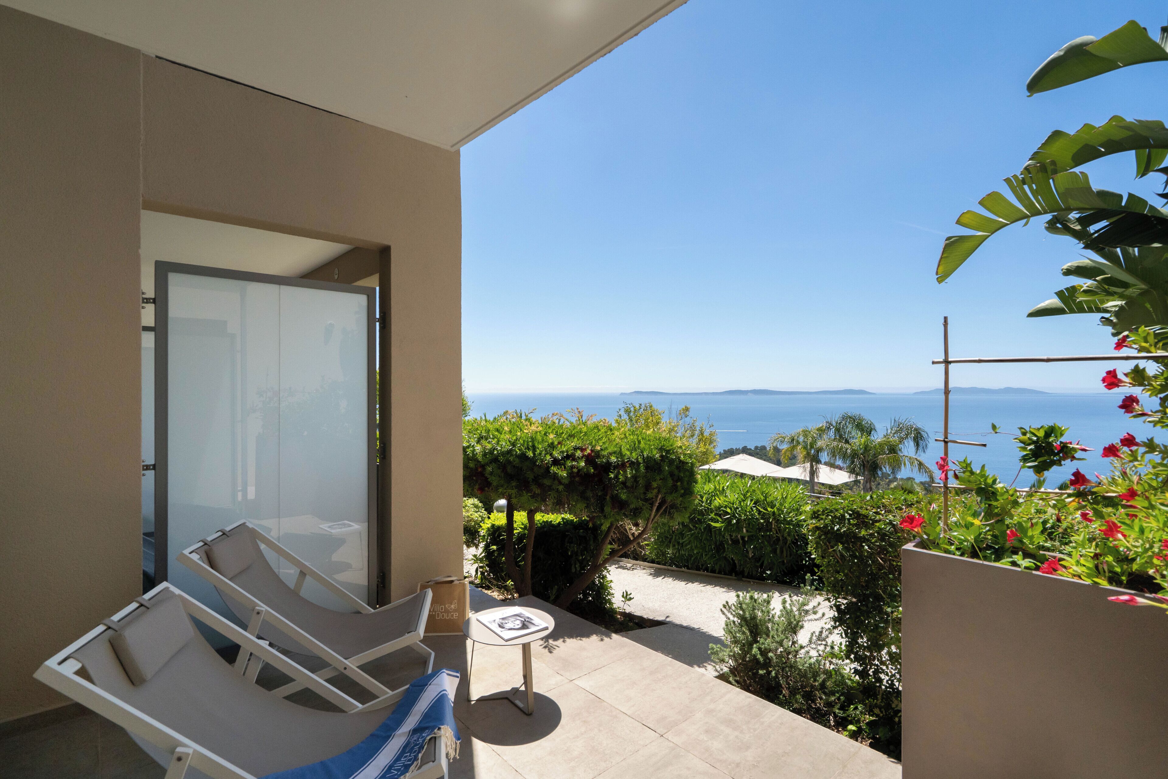 A balcony with two lounge chairs, a small table, and a view of the sea.