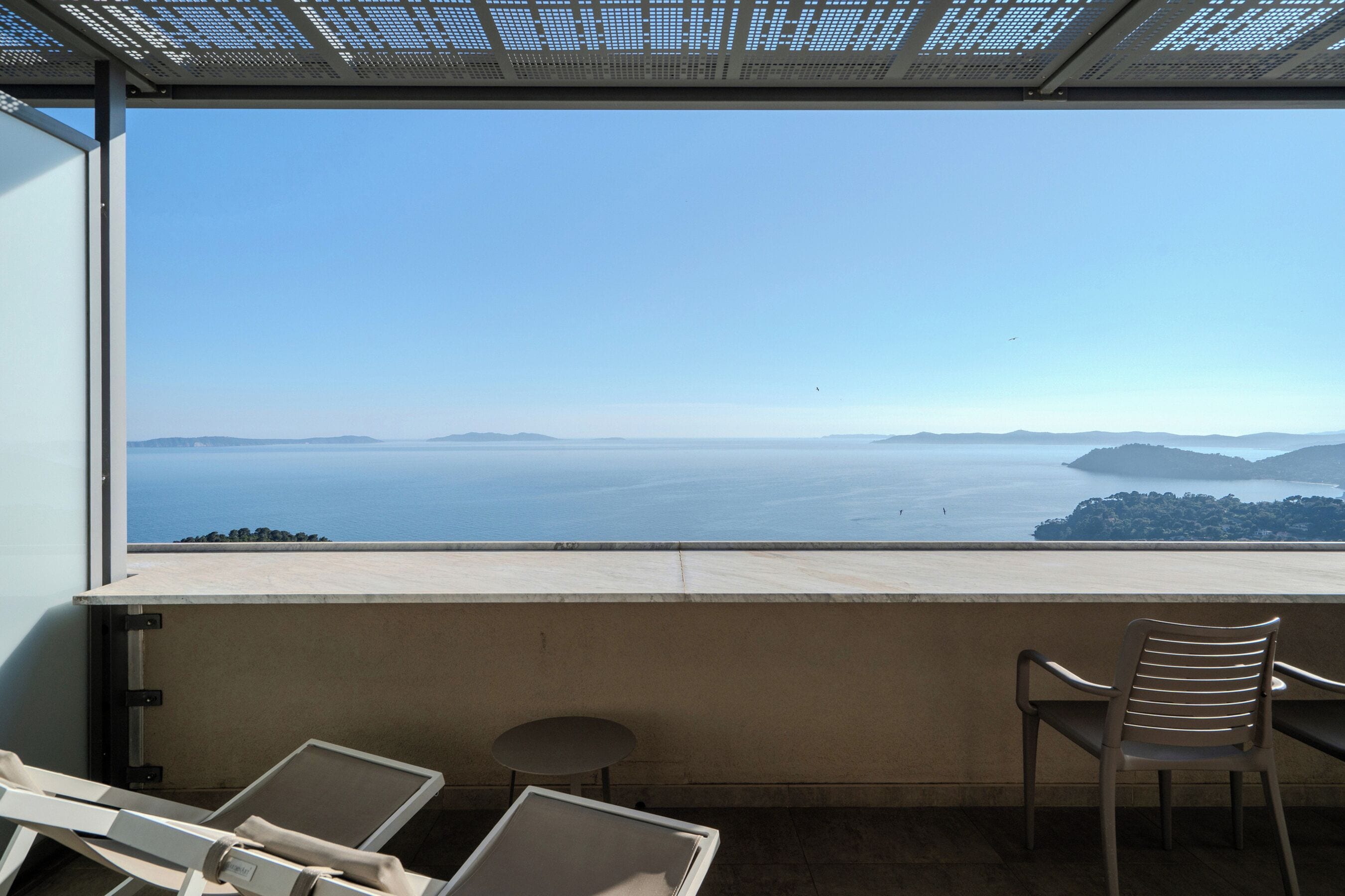 Un balcón con vista al mar, una silla y una mesita.