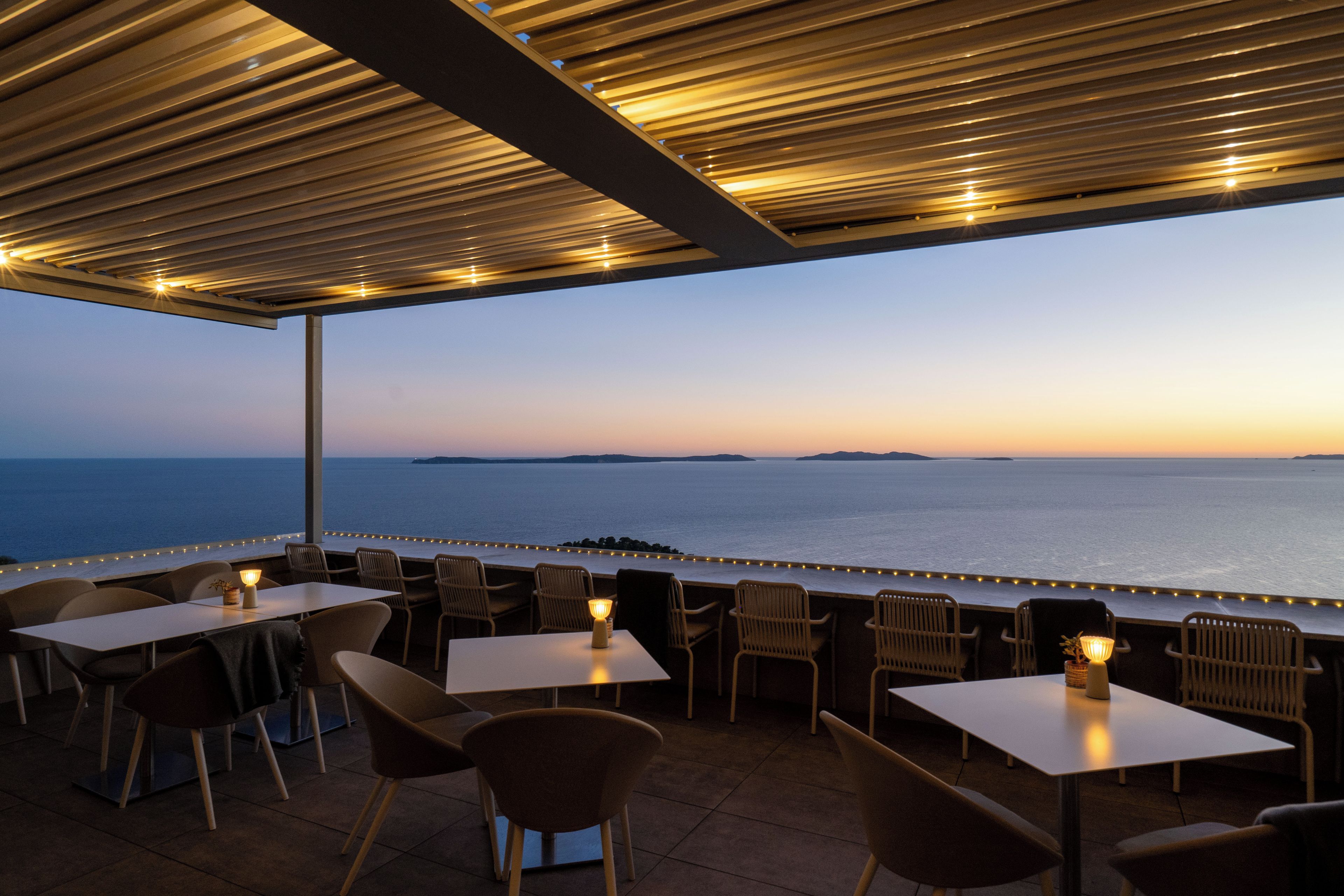 An outdoor seating area with tables and chairs, overlooking a body of water.