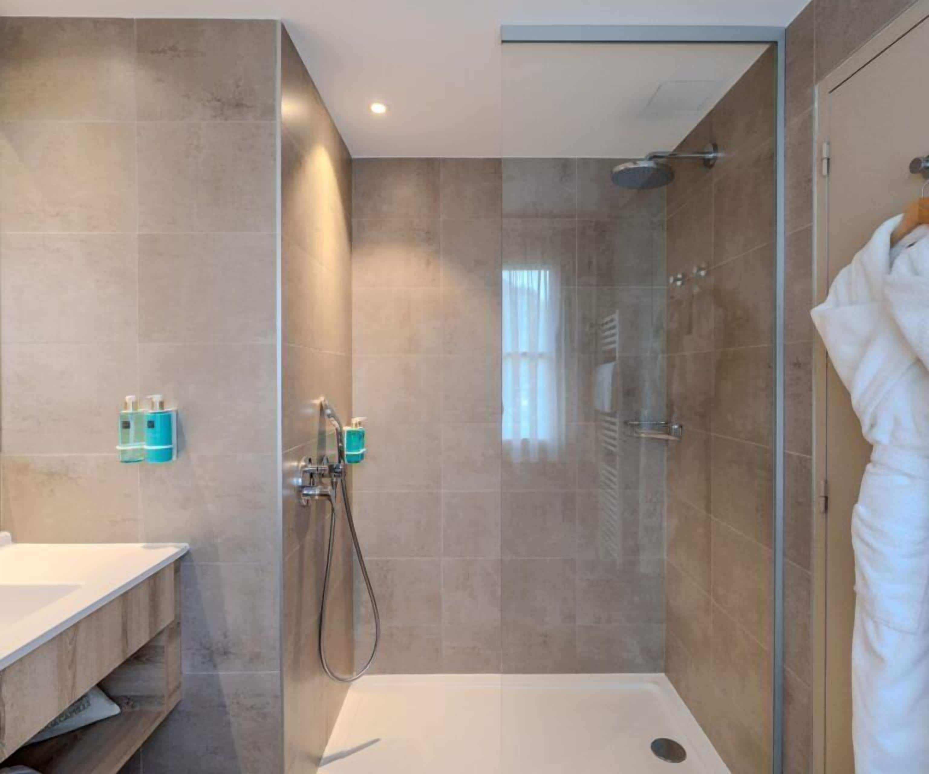 Un baño moderno con ducha envuelta en vidrio, una bañera blanca y un tocador con espejo y lavabo.
