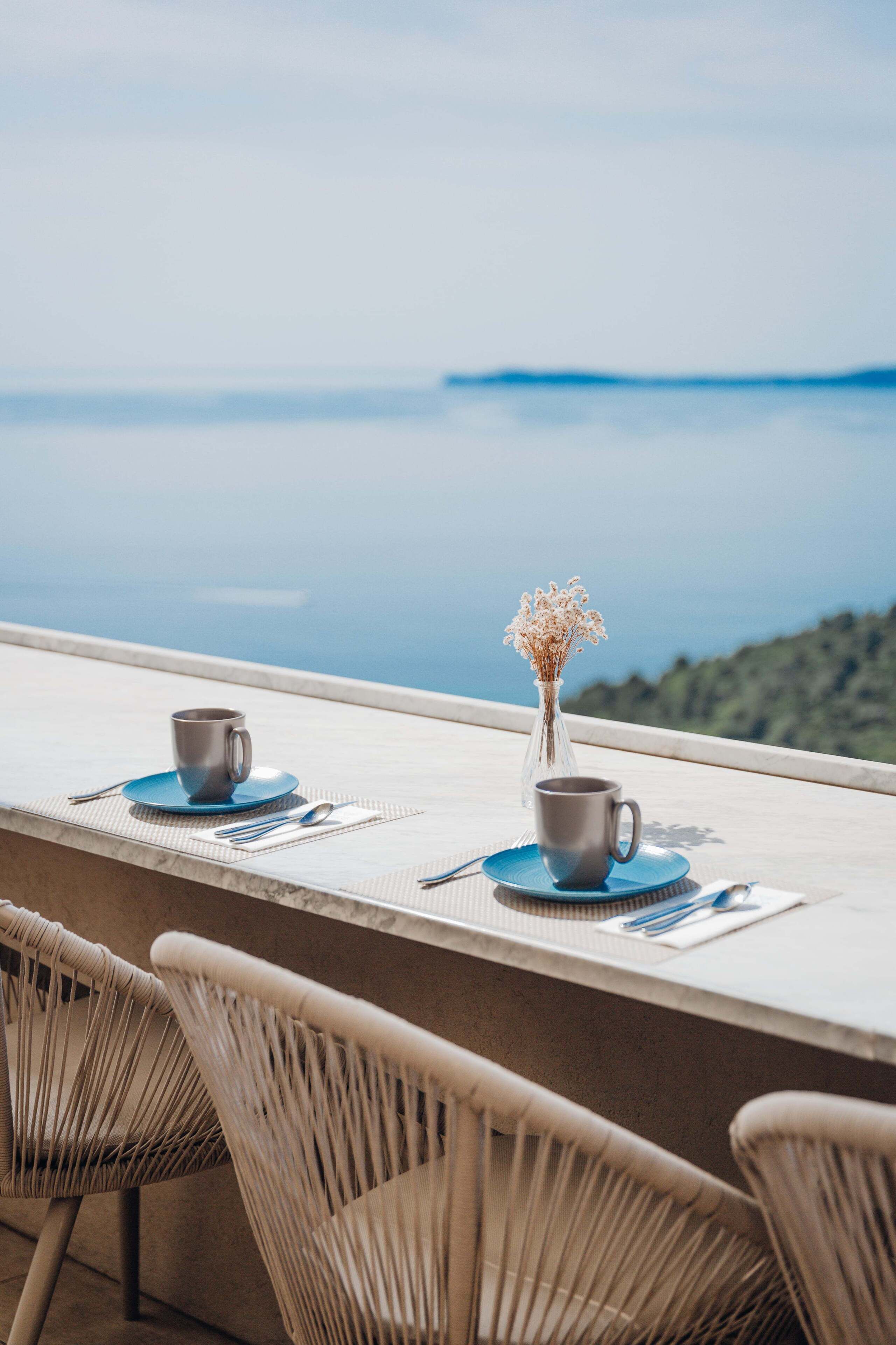 Una terraza con dos mesas, cada una con una taza y platillo, y un florero con flores secas.