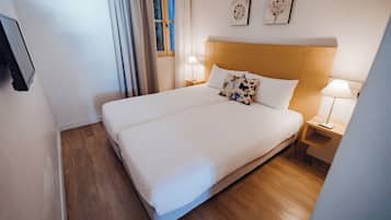 Un lit bien fait, avec du linge de lit blanc, deux tables de chevet avec des lampes et une fenêtre avec des rideaux.