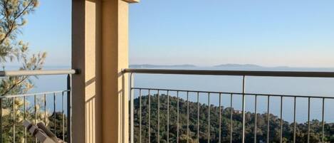 A balcony with a view of the sea and hills, a lounge chair, and a railing.