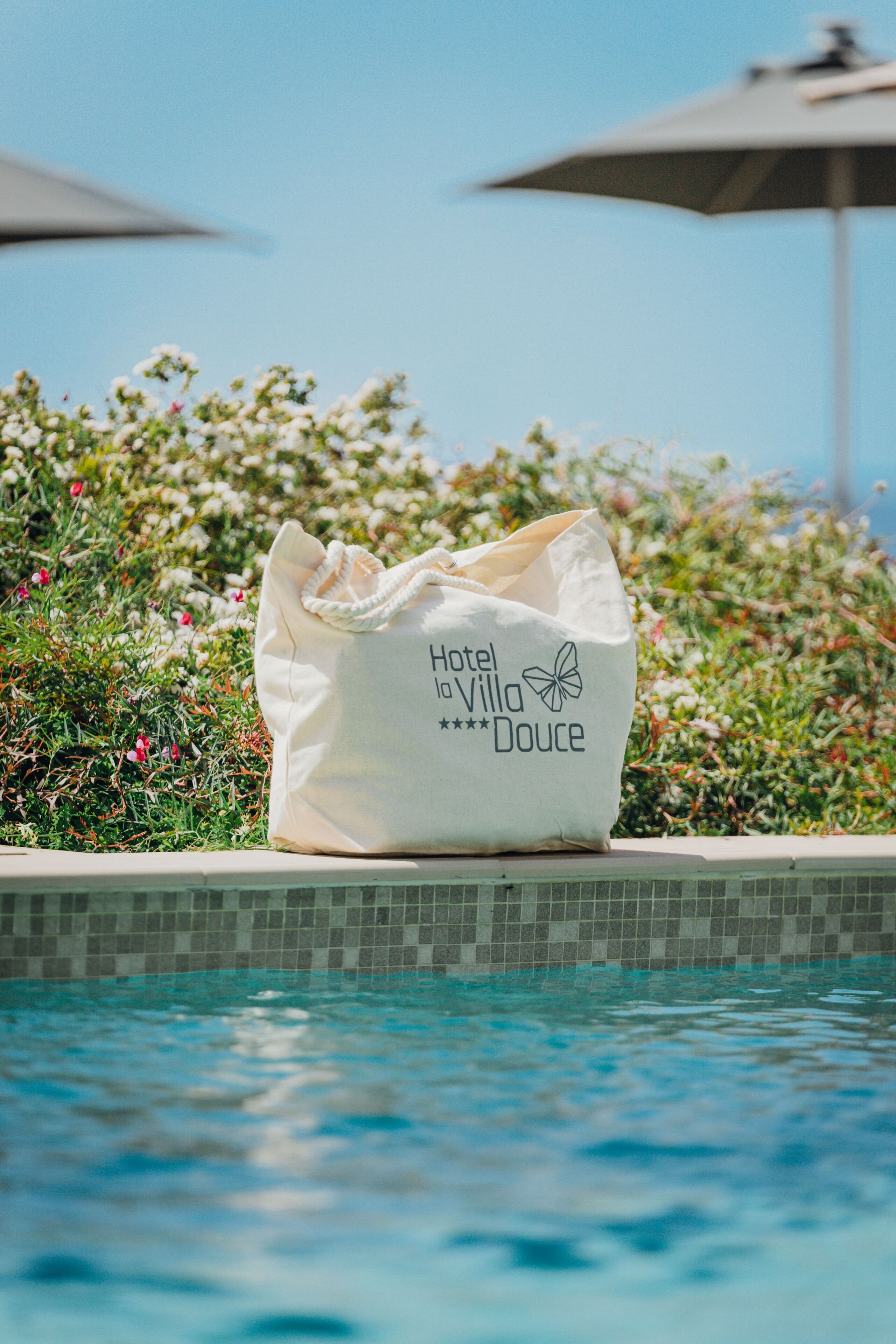 A white bag with the text "Hotel de Villa Douce" placed on a tiled pool edge.