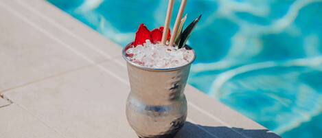 A drink with a straw and a red garnish in a metal cup on a poolside.