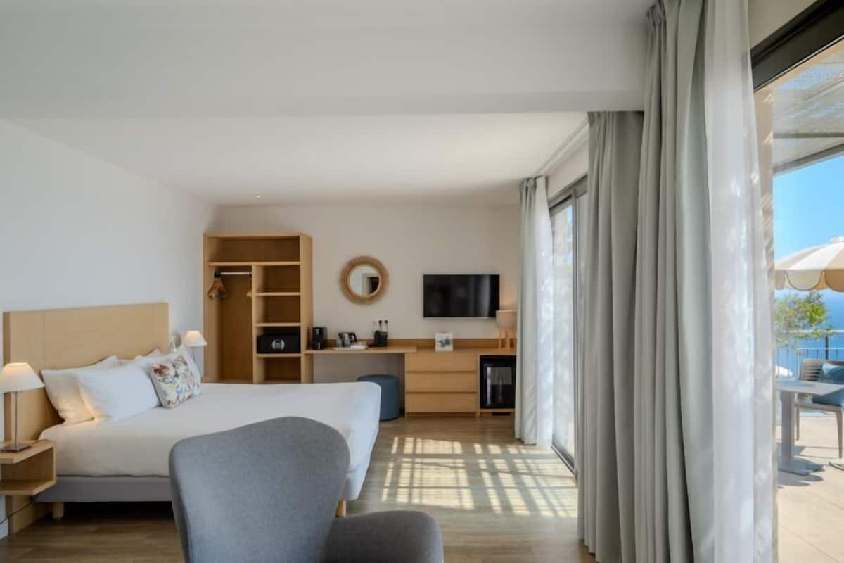 A hotel room with a bed, a desk, a TV, and a view of the outdoors.