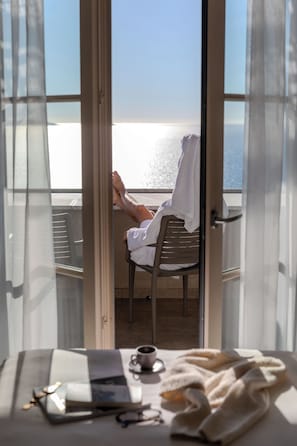 A person relaxing on a chair with a view of the sea through a glass door. - Hôtel La Villa Douce (Rayol-Canadel-sur-Mer)