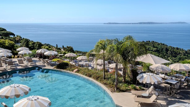 A poolside area with lounge chairs and umbrellas, overlooking a body of water and distant land. - Hôtel La Villa Douce (Rayol-Canadel-sur-Mer)