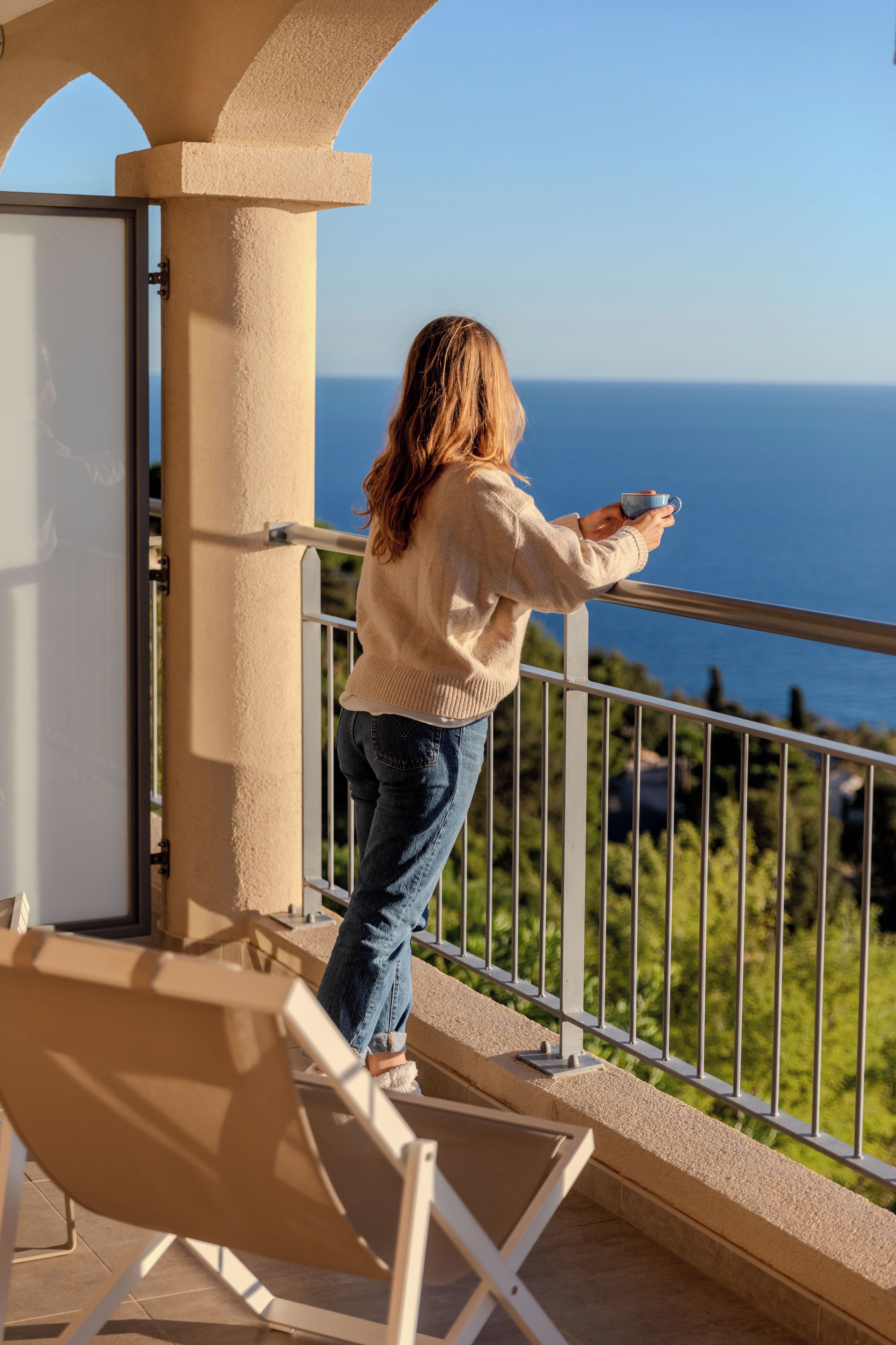A person standing on a balcony with a view of the sea.
