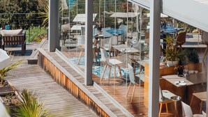 A modern outdoor dining area with a view of the sea, featuring glass walls, wooden flooring, and outdoor furniture. - Hôtel La Villa Douce (Rayol-Canadel-sur-Mer)