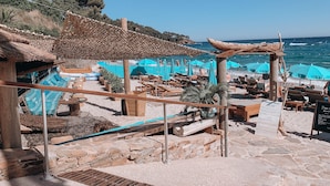 A beachside restaurant with outdoor seating, stone walls, and a view of the sea. - Hôtel La Villa Douce (Rayol-Canadel-sur-Mer)