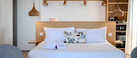 Habitación de hotel moderna con una cama grande, cabecera de madera, mesitas de noche, un banco y una lámpara colgante.