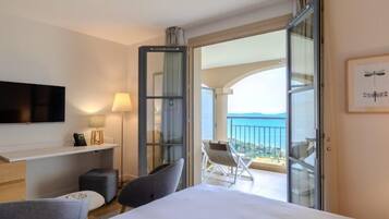 Une chambre d’hôtel comprenant un lit, une télévision, un bureau avec une lampe, une chaise et un balcon avec vue sur la mer.
