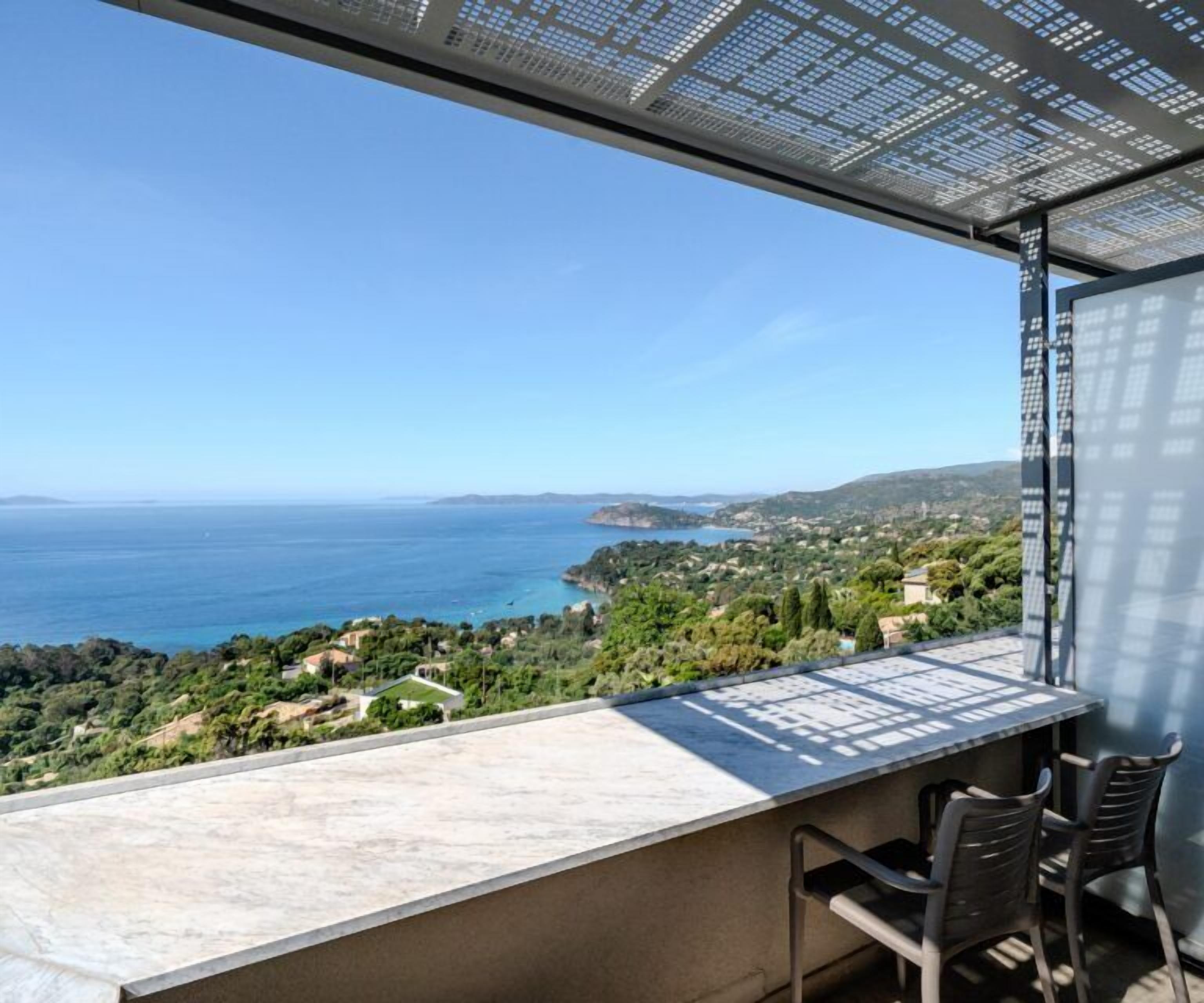 A terrace with a view of the sea and hills, featuring a table and chairs.