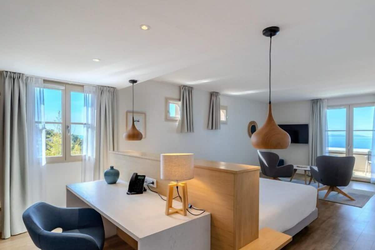 A modern hotel room with a large bed, a desk with a lamp, a chair, and a TV.