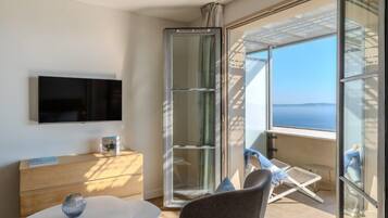 Une chambre d’hôtel moderne dotée d’un balcon, d’une télévision à écran plat, d’une petite table avec un vase et d’un canapé.