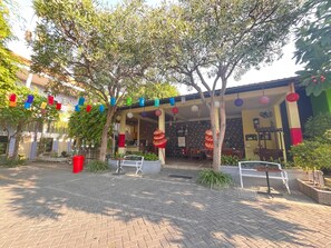 An outdoor patio area with brick flooring, potted plants, and a covered seating area with tables and chairs.