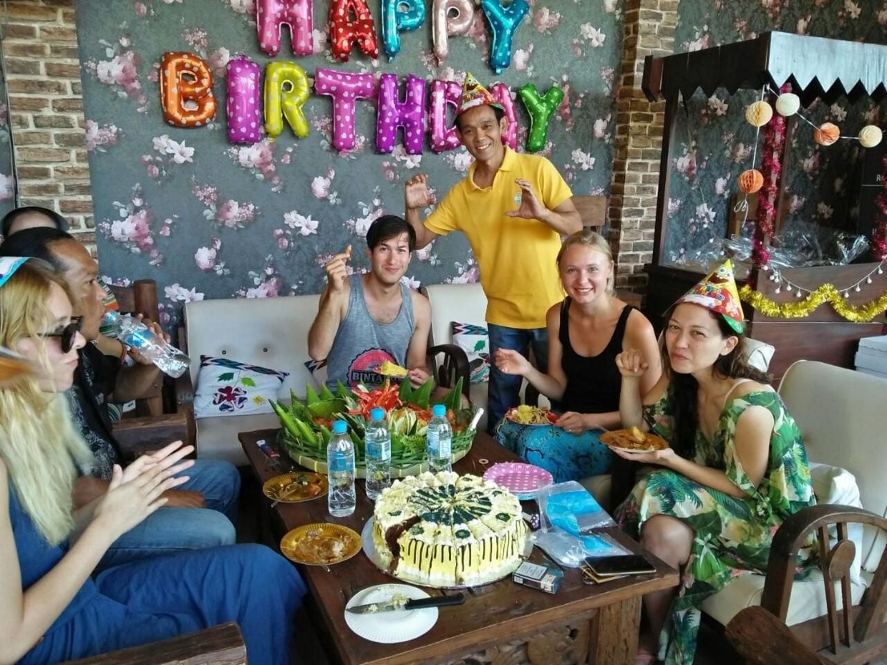 Un gruppo di persone festeggia un compleanno con una torta e palloncini su un tavolo.