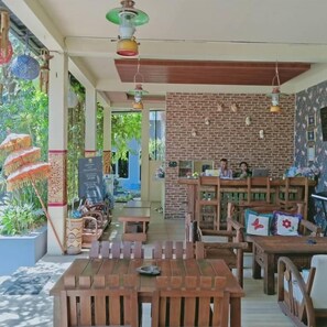 An indoor dining area with wooden tables and chairs, a brick wall, and hanging lights.