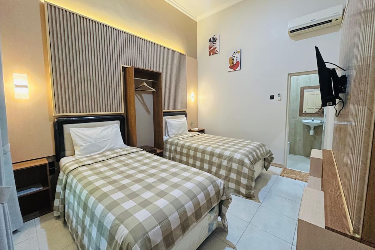 A hotel room with two beds, a wardrobe, a mirror, and an air conditioning unit.