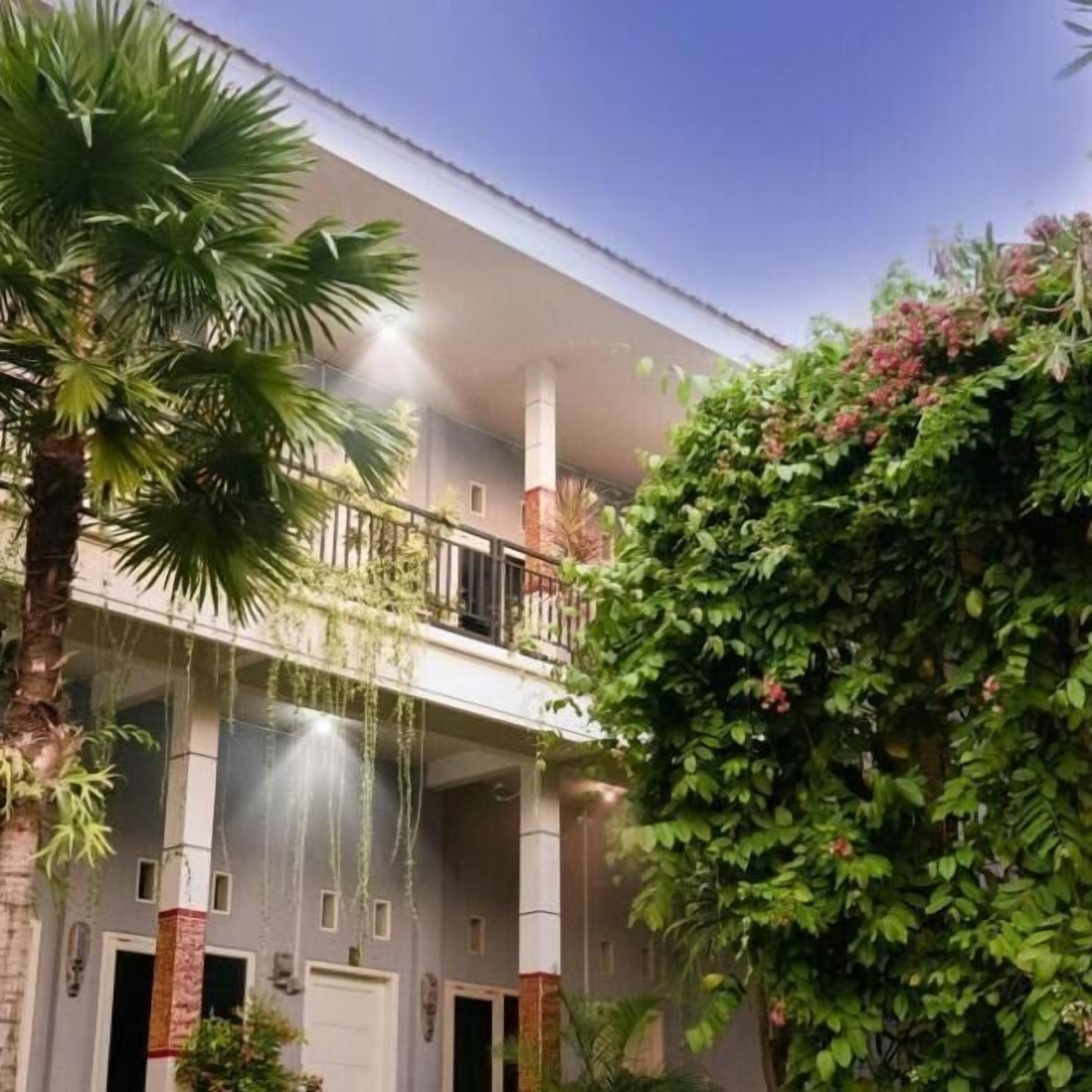 A multi-story building with balconies, a covered outdoor area, and lush greenery.