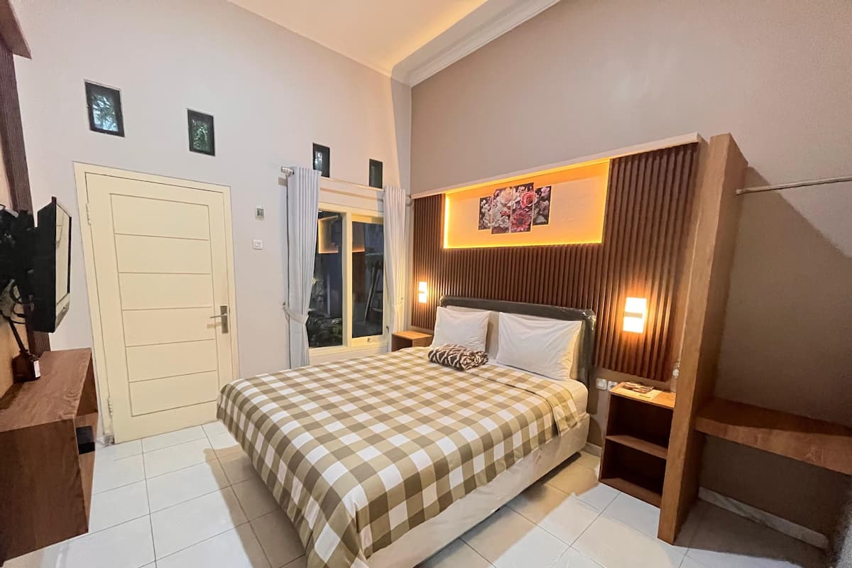 A hotel room with a checkered bedspread, a wooden headboard, two bedside lamps, and a door leading to a balcony.