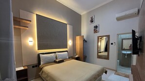 A modern hotel room with a large bed, bedside tables, a wall-mounted light, a mirror, and a bathroom visible through a glass door. - Clover Homestay (Probolinggo)