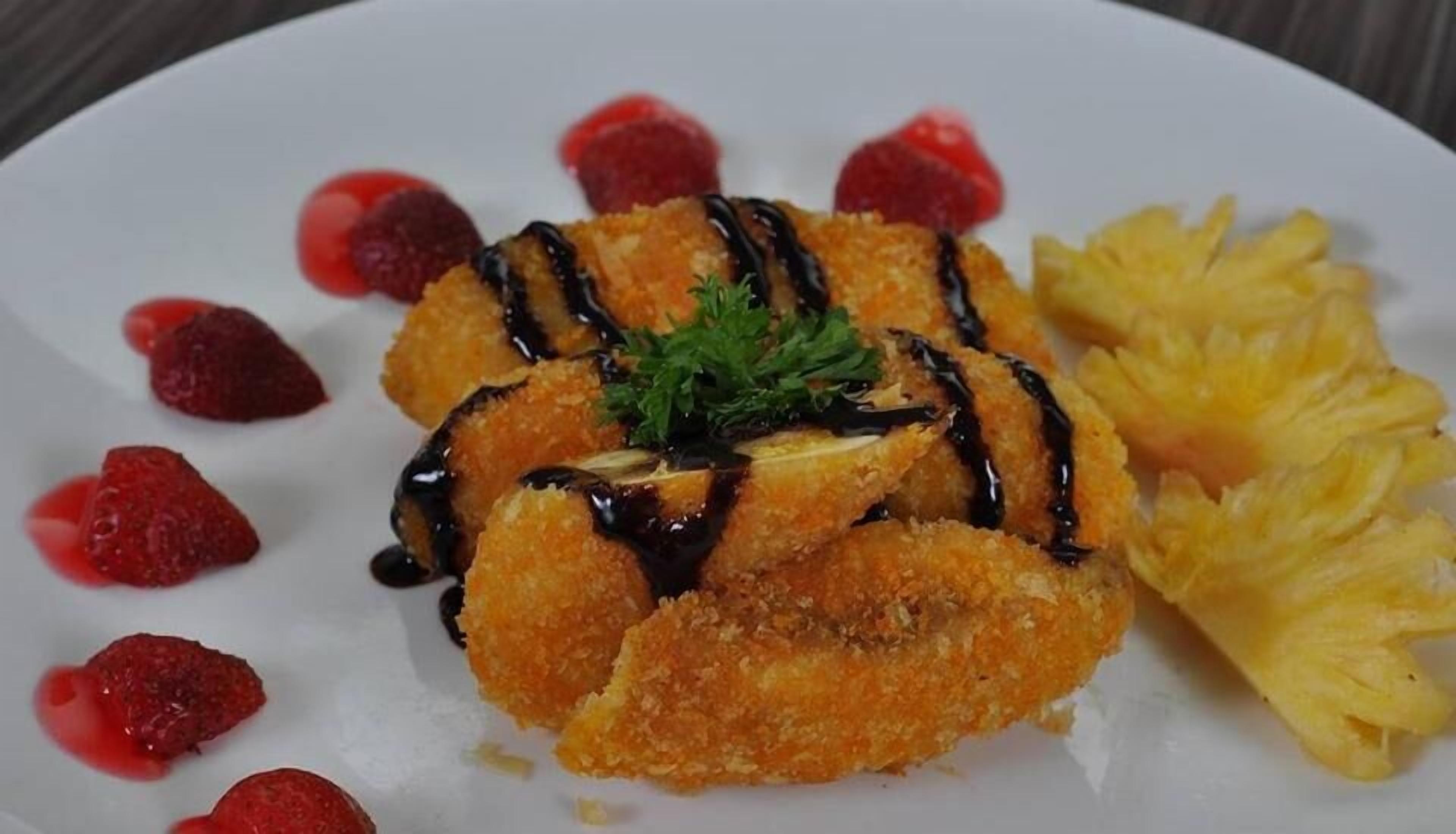 A plate with a breaded item, possibly a chicken cutlet, garnished with parsley and drizzled with a dark sauce, accompanied by strawberries and pineapple.