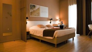 Una habitación de hotel con cama, lámparas de noche, mesita de noche, una silla y una ventana con cortinas.