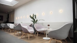 Un área de espera moderna con sillas contemporáneas, una pequeña mesa e iluminación ambiental en la pared.