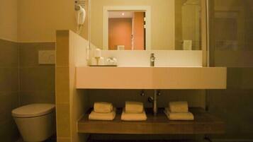 Une salle de bain avec un grand miroir, un lavabo et des toilettes. Des serviettes sont posées sur le plan du lavabo.