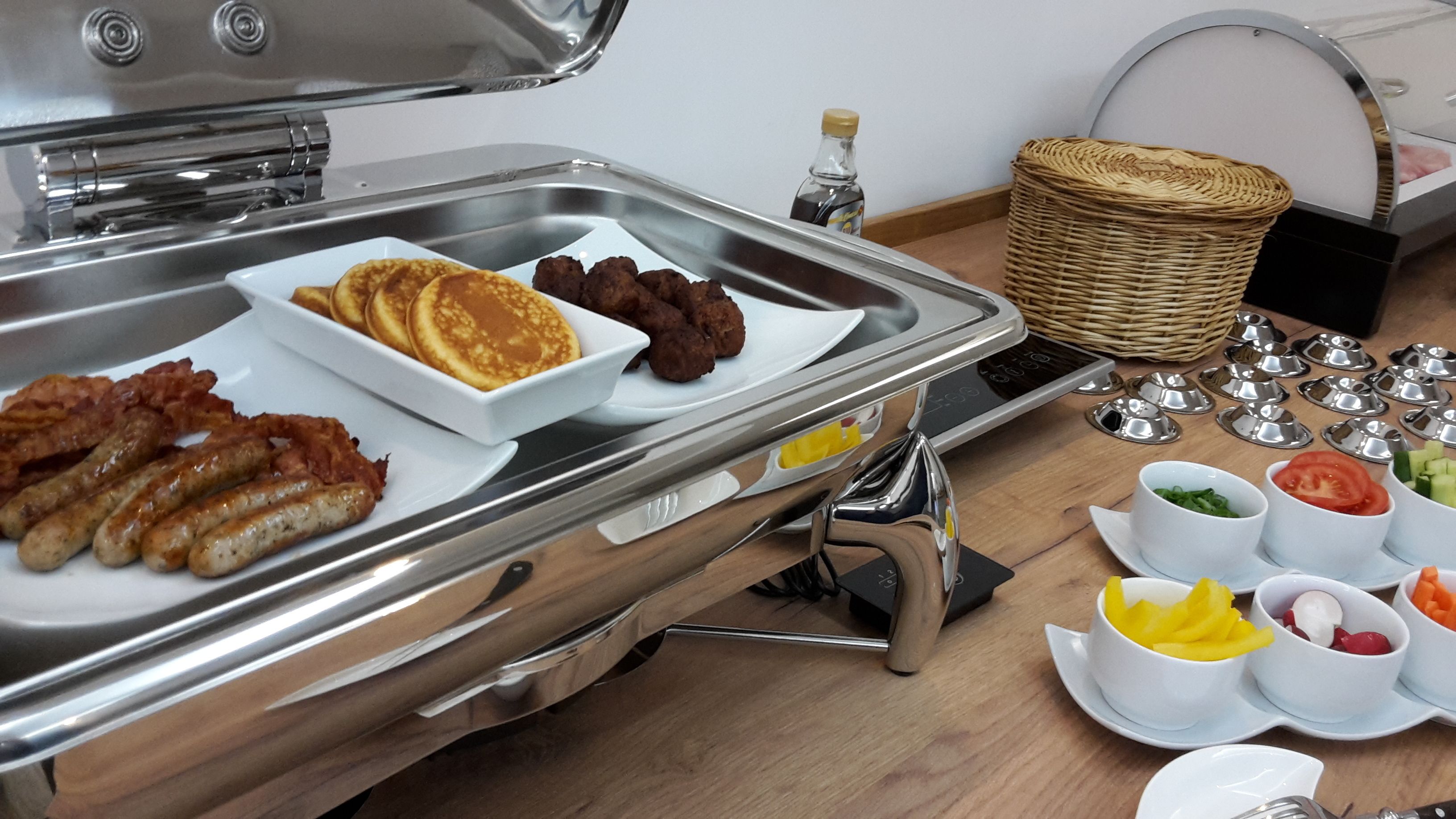 Un buffet con diversi articoli per la colazione, tra cui pancakes, salsicce e polpette.