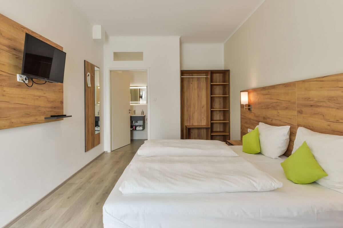 A modern hotel room with a large bed, wooden headboard, a flat-screen TV mounted on the wall, and a walk-in closet.