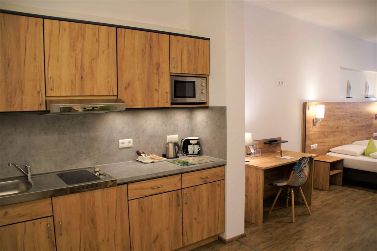 A compact kitchen with wooden cabinets, a microwave, and a coffee maker. There is a small dining area with a table and chair.