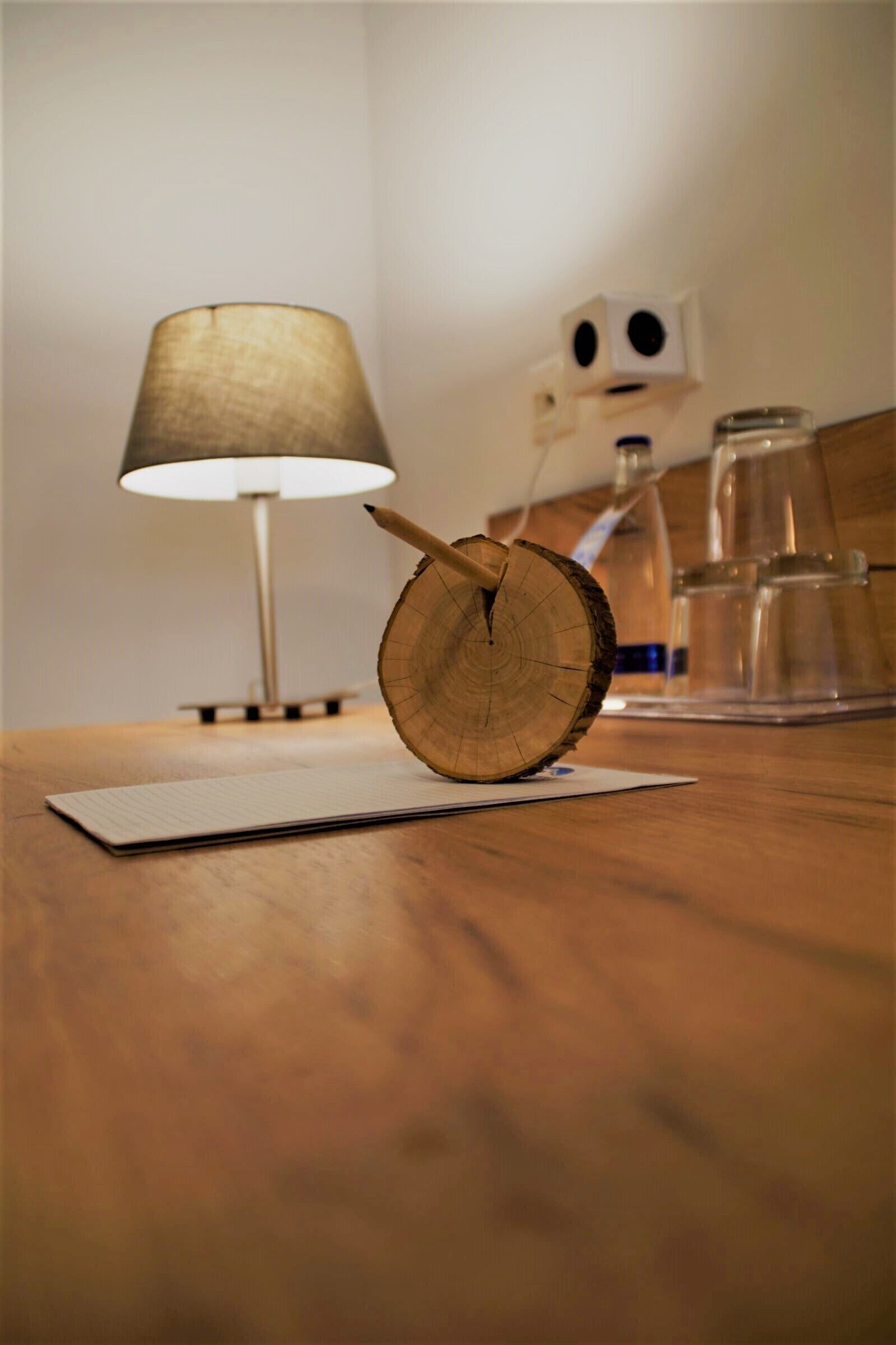 A wooden table with a notepad, a pencil, and a wooden slice. A lamp and a coffee maker are in the background.