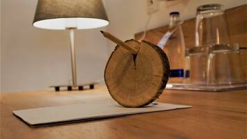 A wooden table with a notepad, a pencil, and a wooden slice. A lamp and a coffee maker are in the background.