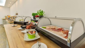 En buffet med forskellige retter, herunder fisk, kød og grøntsager, anrettet på et træbord med et glasmontre.