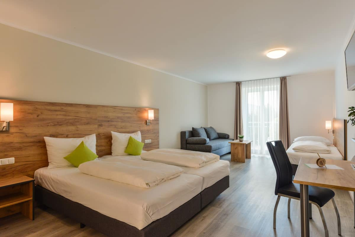 A hotel room with a large bed, a desk, a chair, and a sofa.
