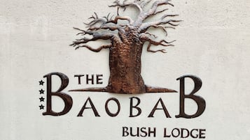 A wall-mounted sign with a tree design and the text "The Baobab Bush Lodge".